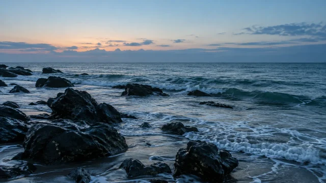 夜明け前の海辺と黒い岩の風景